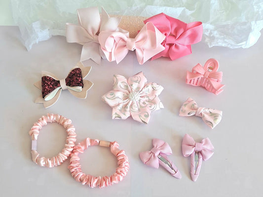 Set of pink baby hair accessories including headband bows, flower clip, glitter bow, scrunchies, snap clips and claw clip on white background